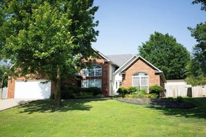 A single-story house with a garage, a front yard with a tree, and a wooden fence. - Walking distance to Coler MTN Bike - 3BR 2BA (Bentonville)