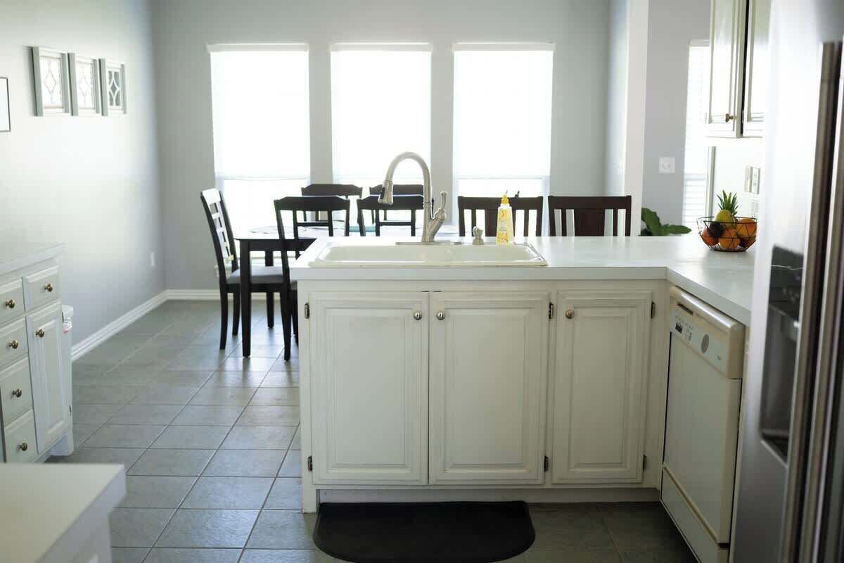 A kitchen with white cabinets, a sink, and a dining area with chairs.