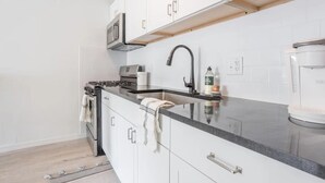Una cocina moderna con armarios blancos, encimera negra, estufa, fregadero y cafetera.