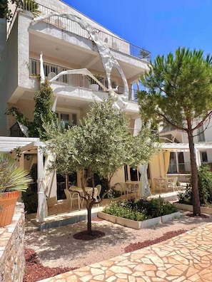 A multi-story building with balconies, outdoor seating, and a tree in the courtyard. - Most Oliva Resort Budva (Pržno)