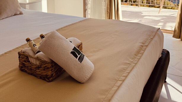 Een hotelkamer met een bed, een klein tafeltje en uitzicht op een bergachtig landschap vanuit een open balkon.