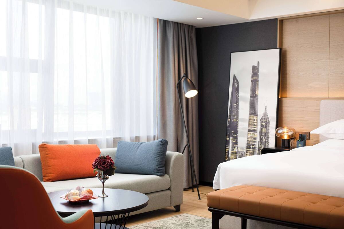 Una habitación de hotel con cama, sofá, mesa de centro y lámpara.