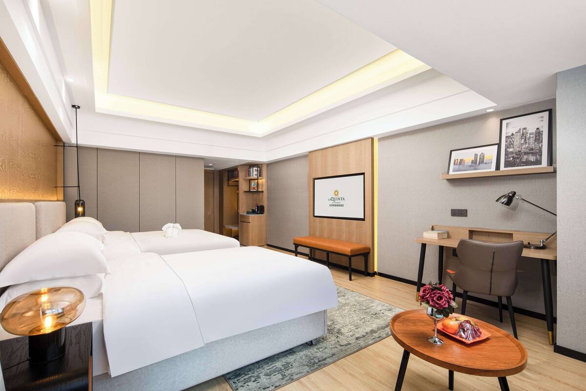Una habitación de hotel moderna con una cama grande, un escritorio, una silla y una mesita con un jarrón de flores.