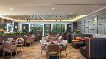 A restaurant with round tables and booths, large windows, and indoor plants.