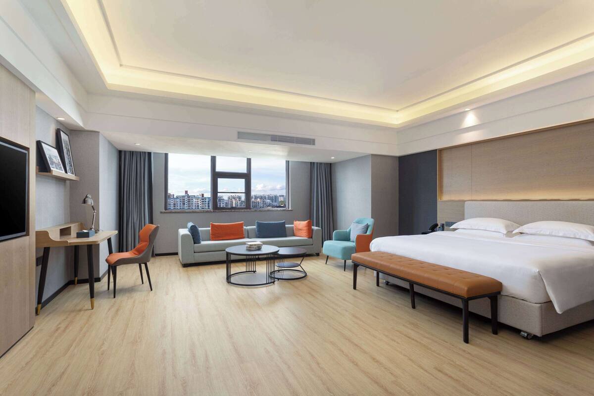 Una habitación de hotel moderna con una cama grande, un sofá, un escritorio y vistas a la ciudad.