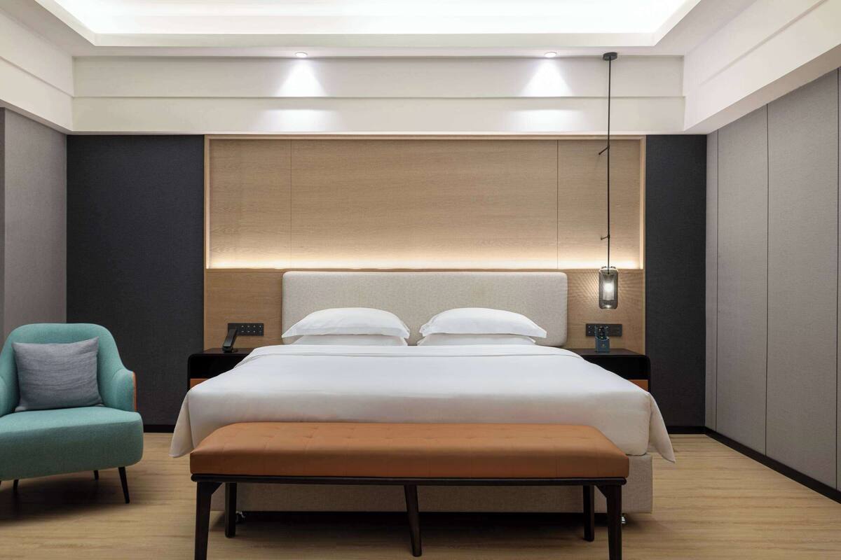 Una habitación de hotel moderna con una cama grande, una mesita de noche, una silla y un banco.