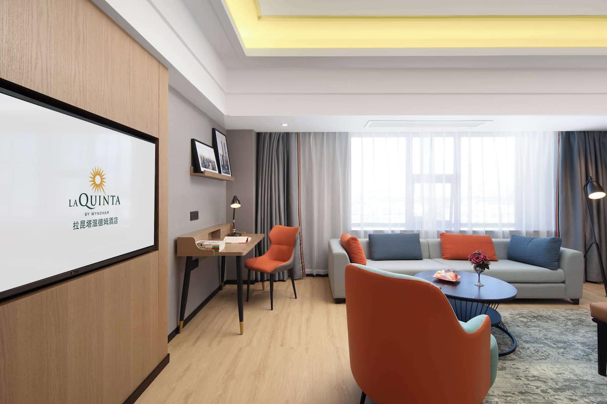 Una habitación de hotel moderna con una pantalla grande mostrando el nombre del hotel, un conjunto de sofás, una mesa de comedor y una mesa de centro.