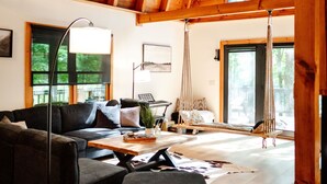 Un salón amplio con techo alto, vigas de madera, un ventanal grande, un sofá, una mesa de centro y un sillón colgante.