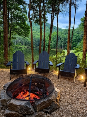 Feuerstelle mit drei Adirondack-Stühlen in bewaldeter Landschaft.