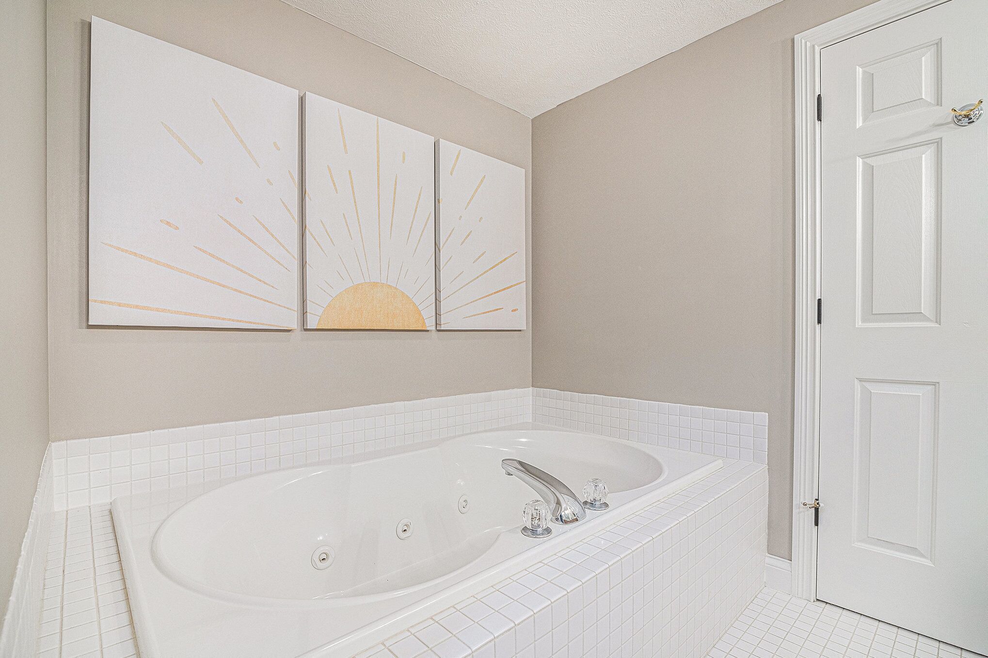 A bathroom with a large bathtub, white tiles, and a door.