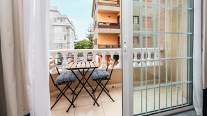 A balcony with a table and chairs, a view of adjacent buildings, and a barred window.