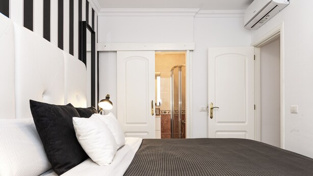 A hotel room with a large bed, a bedside table with a lamp, a wardrobe, and a bathroom visible through an open door.