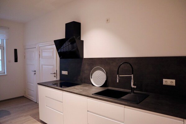 A modern kitchen with a black countertop, white cabinets, a black sink, and a stainless steel range hood.