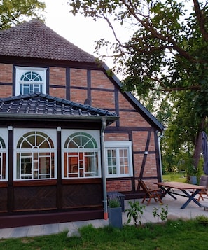 A traditional half-timbered house with a tiled roof, large arched windows, and a patio area with outdoor seating.
