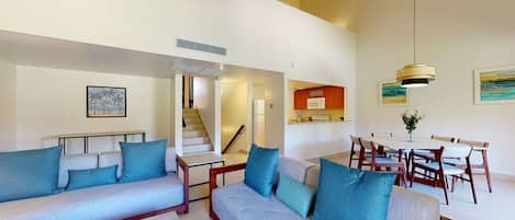 Amplia sala de estar con un conjunto de sofás, una mesa de comedor con sillas y una escalera que conduce a un nivel superior.