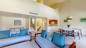 Amplia sala de estar con un conjunto de sofás, una mesa de comedor con sillas y una escalera que conduce a un nivel superior.