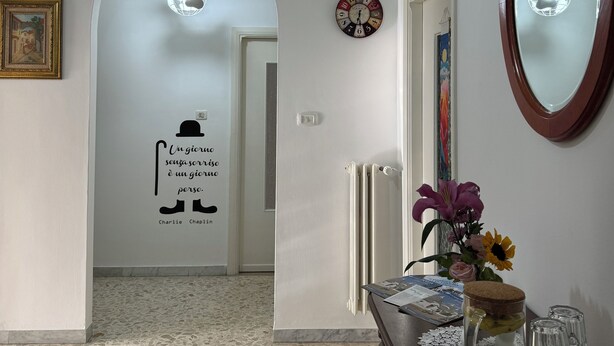 Un couloir avec un luminaire en forme de globe, une horloge, une citation affichée sur le mur et un vase décoratif posé sur une table.