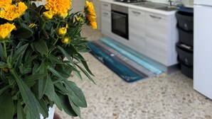 Une cuisine moderne avec des meubles blancs, une cuisinière et un réfrigérateur. On aperçoit, au premier plan, un pot de fleurs contenant des fleurs jaunes.