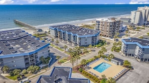 Um hotel à beira-mar com vários edifícios, estacionamento, piscina e um cais ao fundo.