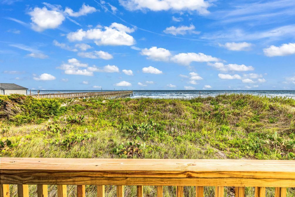 A wooden deck overlooking a beach with a pier extending into the ocean.