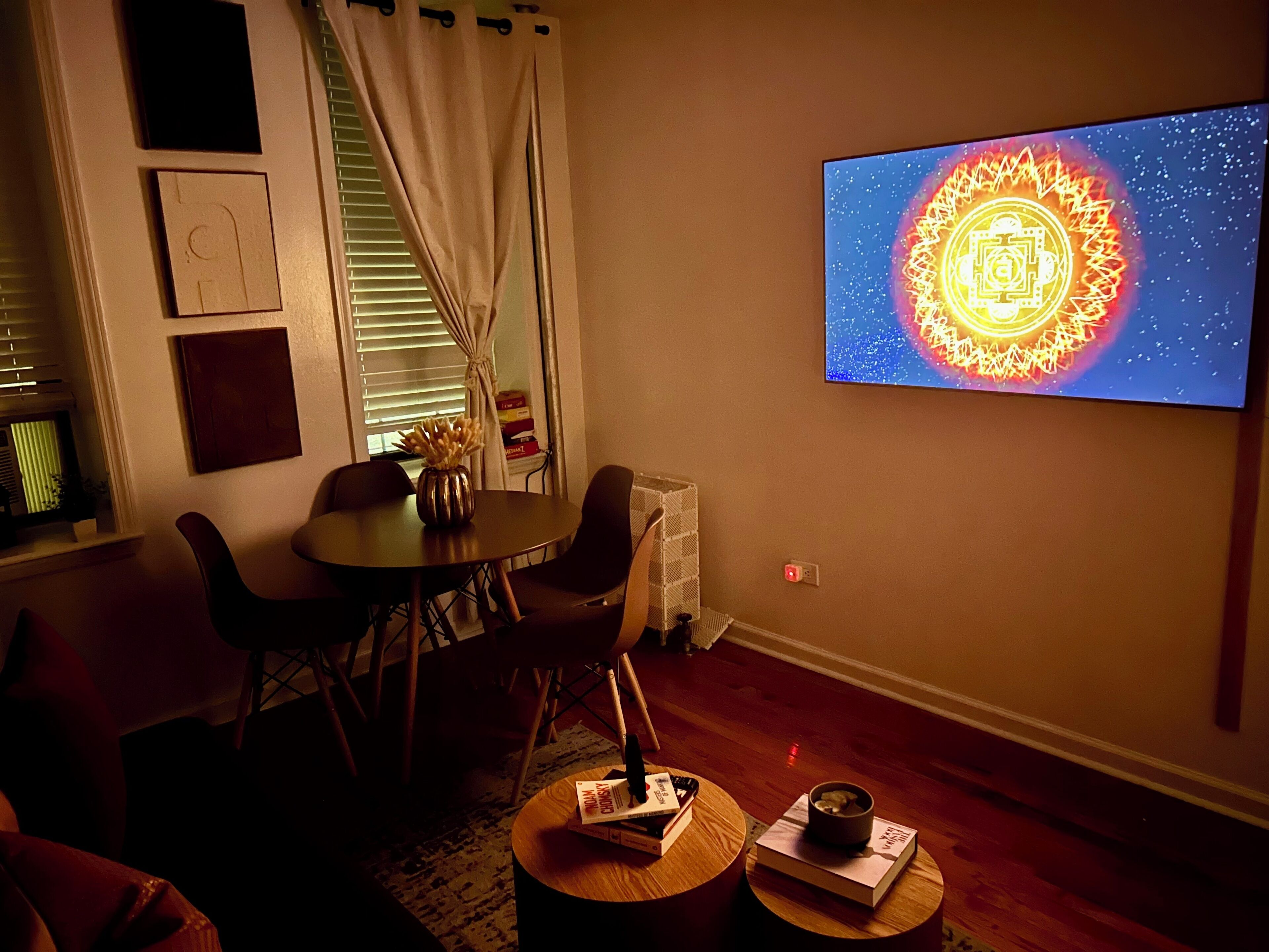Ein Wohnzimmer mit Esstisch, Stühlen, Couchtisch und einem Flachbildfernseher, der eine Mandalas zeigt.