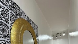 Un pasillo con papel tapiz estampado, un espejo con marco dorado y una puerta blanca al final.