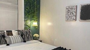 Una cama bien hecha con colcha de cuadros blancos y negros, una pared verde y dos obras de arte colgadas.