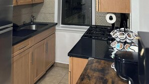 Una cocina con armarios de madera, un refrigerador de acero inoxidable, una encimera negra, una ventana y una estufa.