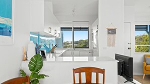 A modern kitchen with a central island, large windows, and a view of the outdoors. - 4-53 Forsters Bay Road, Narooma - Blue Water Villas (Narooma)