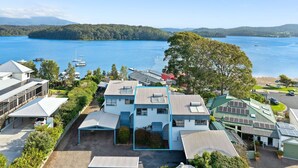 A residential area with houses featuring solar panels, a large tree, and a lake in the background. - 4-53 Forsters Bay Road, Narooma - Blue Water Villas (Narooma)