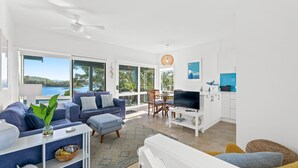 A modern living room with a sofa, TV, and dining area. - 4-53 Forsters Bay Road, Narooma - Blue Water Villas (Narooma)