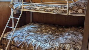 A bunk bed with a leaf-patterned bedspread, a wooden wall, and a window with curtains.