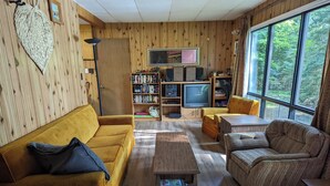 A cozy living room with a yellow sofa, a brown armchair, and a wooden coffee table. A bookshelf filled with books and a television are also visible.