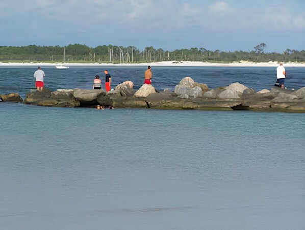 A beach with people standing on rocks by the water.