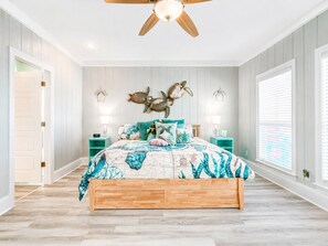A bedroom with a wooden bed, teal and white bedding, decorative wall art, and a ceiling fan.