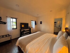 A bedroom with a bed, a television, a window, a mirror, and a door leading to a bathroom.