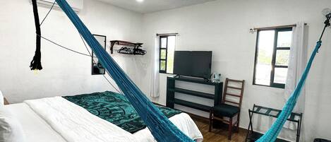Une chambre avec un lit, un hamac, une télévision et une fenêtre.