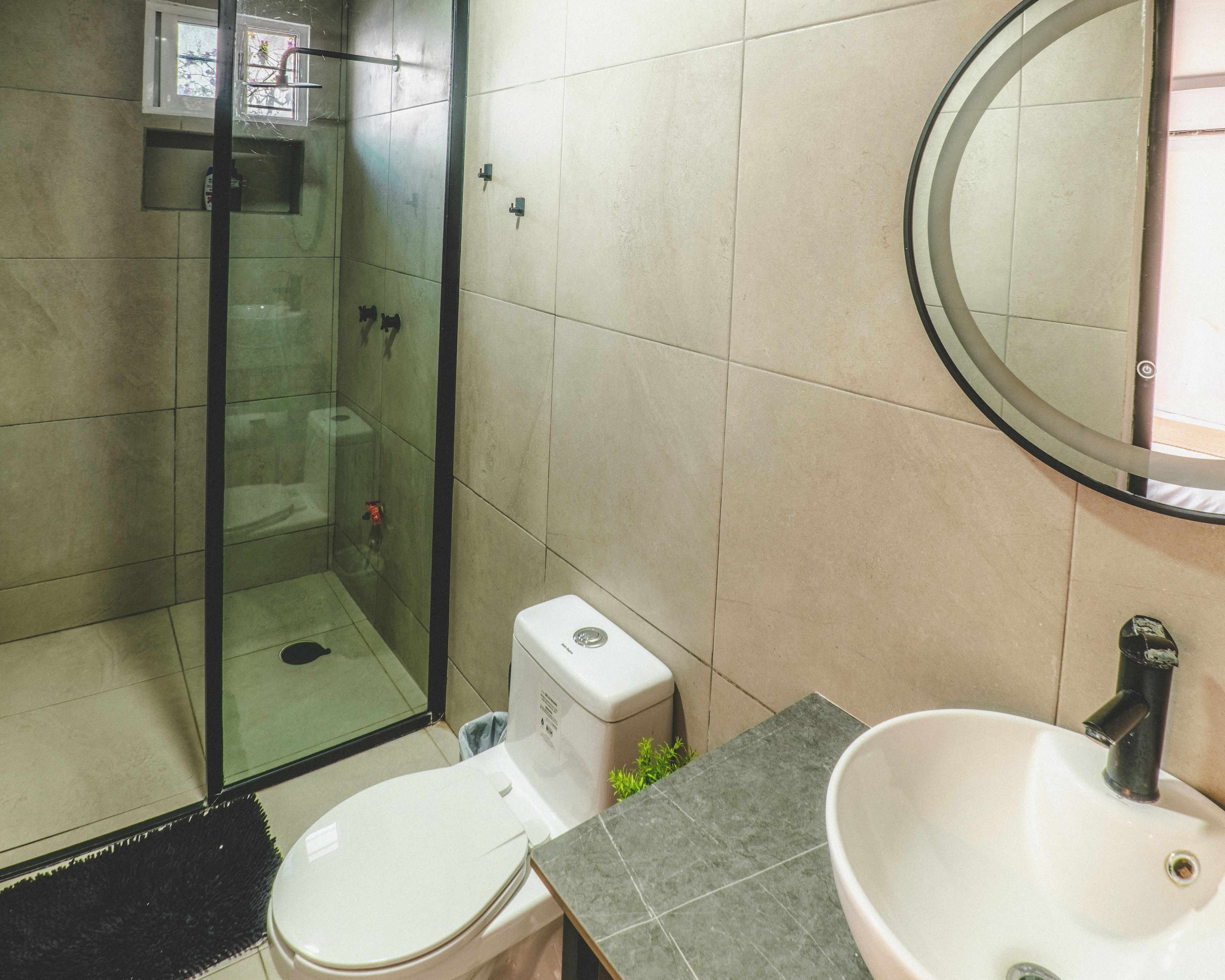 A bathroom with a glass shower enclosure, a toilet, and a sink with a mirror above it.