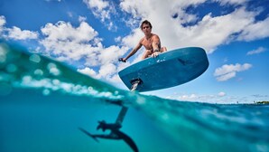 A person surfing on a wave with a clear blue sky and clouds in the background. - La Perle Noire (Cozumel)