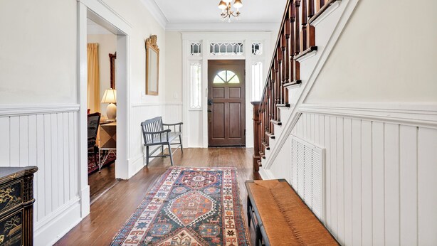 A hallway with a patterned rug, a wooden bench, a chair, and a staircase with a wooden railing. - Going to Carolina! Historic Downtown Wilmington (Wilmington)