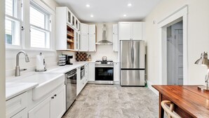 A modern kitchen with white cabinetry, stainless steel appliances, and a wooden dining table. - Going to Carolina! Historic Downtown Wilmington (Wilmington)