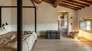 Ein Schlafzimmer mit einem Himmelbett, Holzbalkendecke, einem kleinen grünen Truhenkasten und einem Fenster mit Blick.