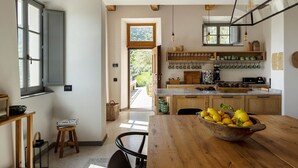 Eine Küche mit Holzausstattung, einem Esstisch mit einer Zitronenschale und Blick in den Garten durch eine offene Tür.