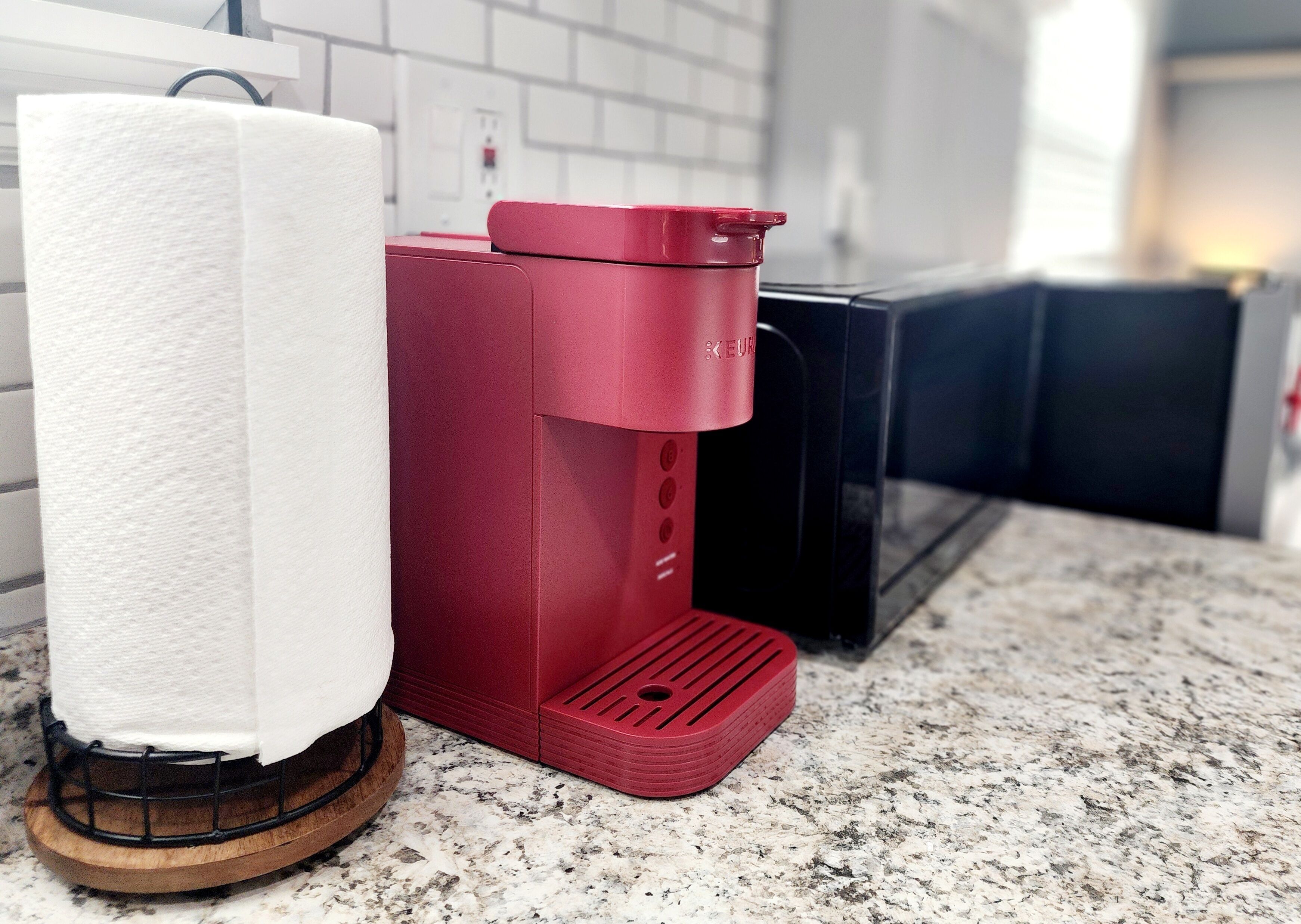 Una cocina con cafetera, dispensador de toallas de papel y un electrodoméstico negro sobre una encimera de granito.
