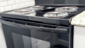 Una cocina con estufa de acero inoxidable, gabinetes blancos y salpicadero de azulejos.