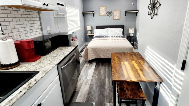 Una habitación compacta con cama, mesitas de noche, un escritorio pequeño y una kitchenette.