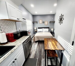 Une chambre à coucher de taille réduite, comprenant un lit, des tables de chevet, un petit bureau et un coin cuisine.
