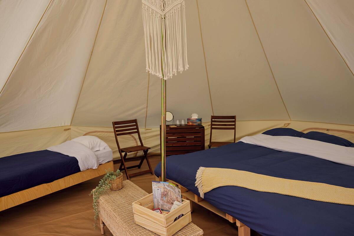 A tent with two beds, wooden furniture, and a hanging macrame light fixture.