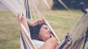 Una persona descansando en una hamaca al aire libre, con una tienda de campaña al fondo.