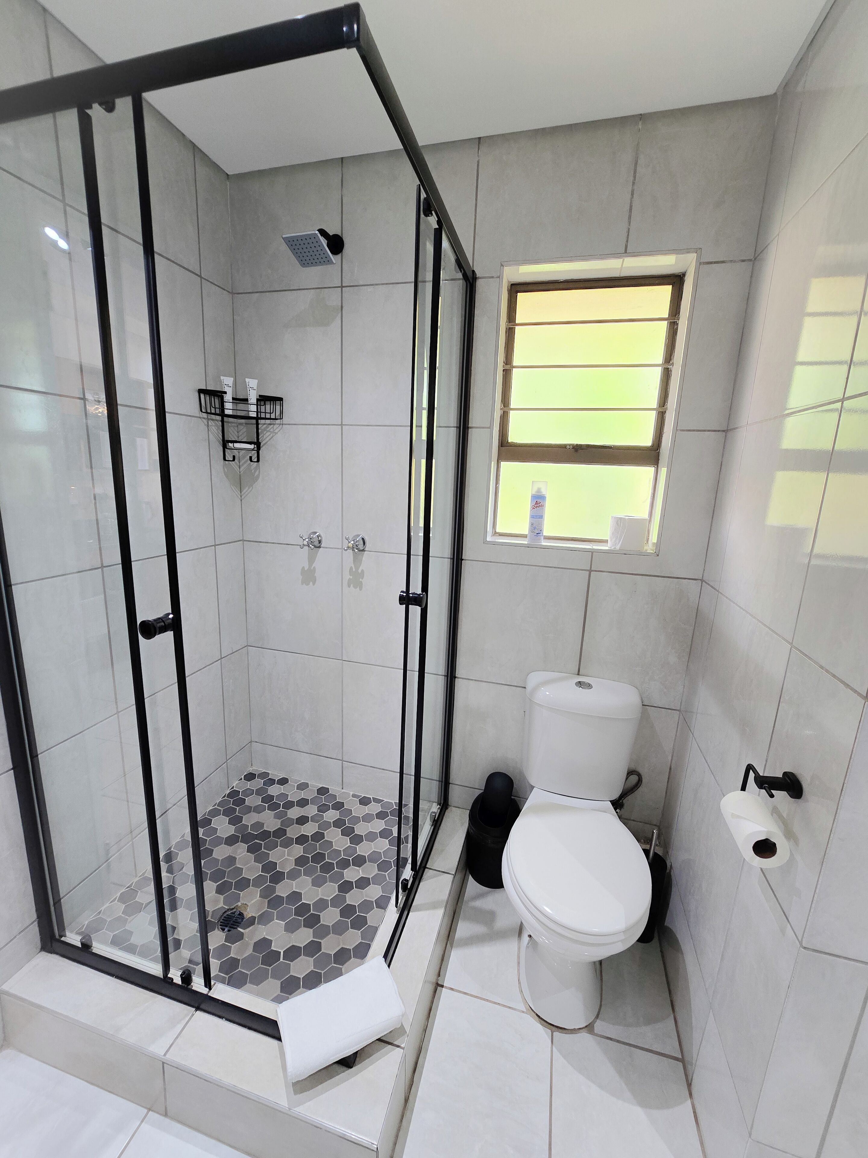 Un baño con ducha envuelta en vidrio, un inodoro y una ventana.